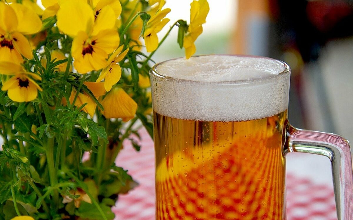 Ein Bier steht neben Blumen auf einem Tisch in einem Biergarten Ein Bier steht neben Blumen auf einem Tisch in einem Biergarten